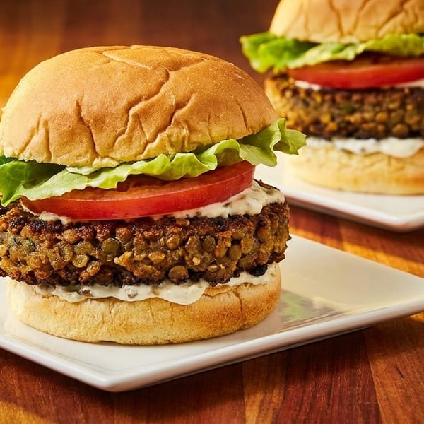 Two delicious veggie burgers with lettuce, tomato, and sauce on white plates.