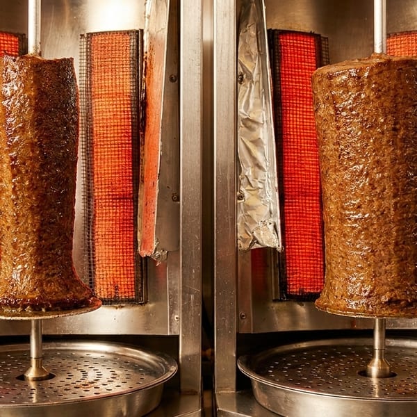 Two large vertical spits of glistening doner kebab meat cooking on a rotisserie with red heating elements.