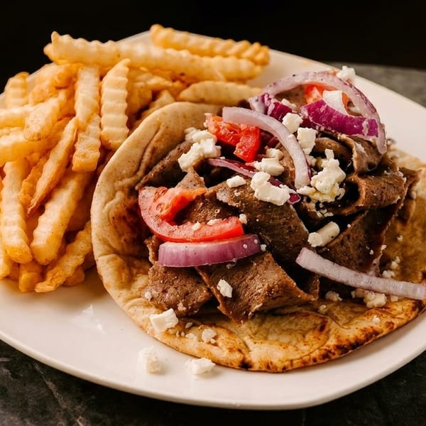 A gyro with meat, tomatoes, red onions, and feta cheese, served with crinkle-cut fries.